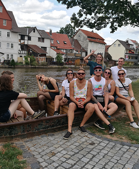 Ein Team von einer Großveranstaltung sitzt entspannt mit Sonnenbrillen in einem Boot, das als Sitzgelegenheit an einem Kanal umfunktioniert wurde