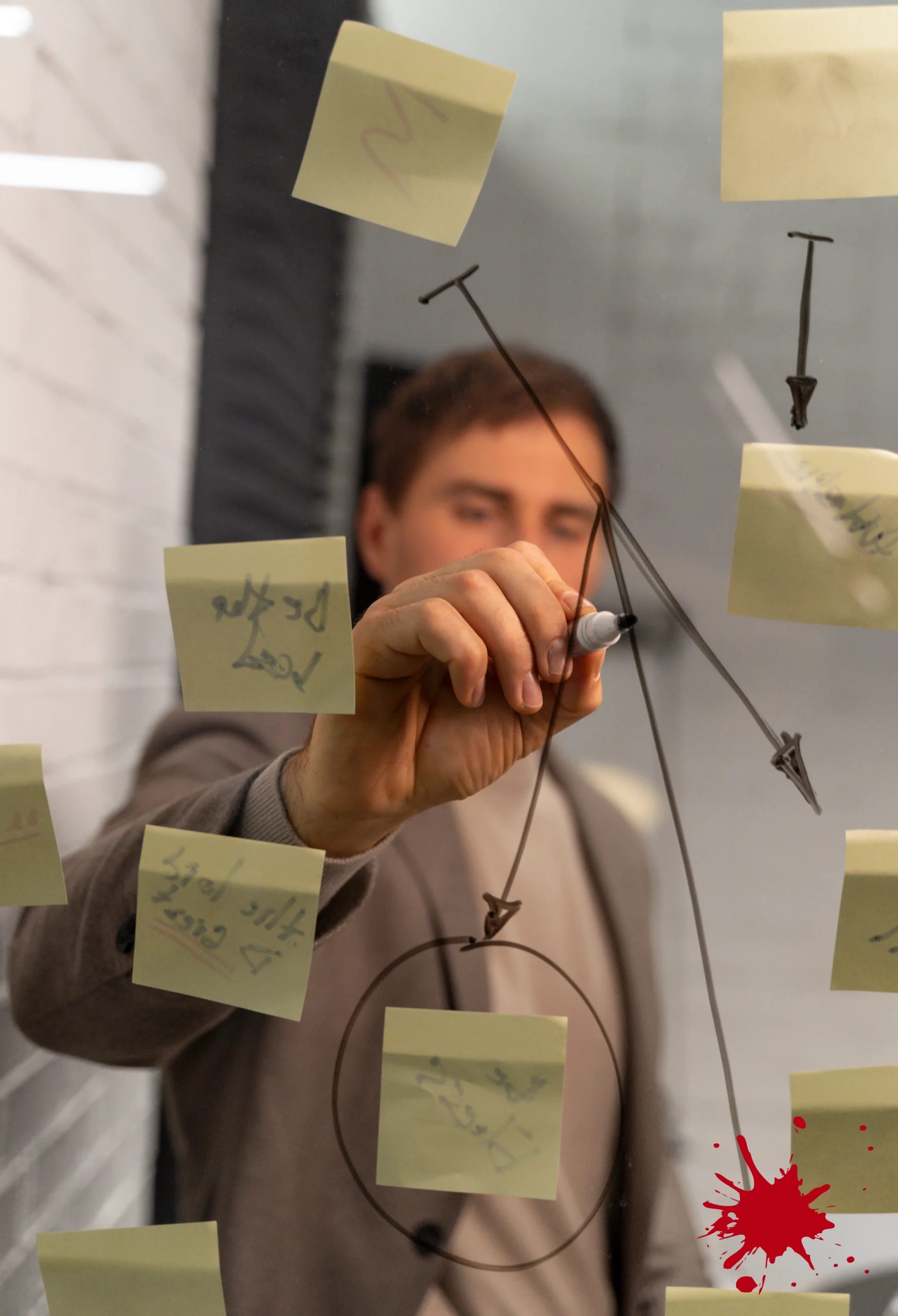 Junger Mann hinter einer Glasscheibe nutzt Stift um Plan zwischen Post its aufzuzeigen