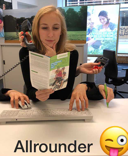 Das Bild zeigt eine Frau am Schreibtisch, die in einem Flyer liest. Um sie herum noch weitere Hände, die telefonieren, schreiben, auf einer Tastatur tippen, die Maus bedienen und stempeln.
