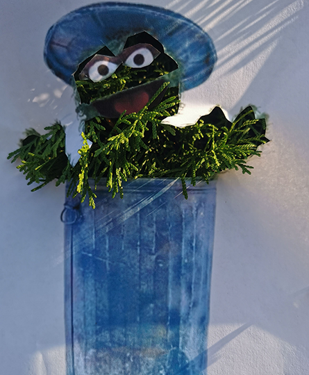 Das Bild zeigt einen Elmo, der aus einer blauen Mülltonne schaut. Elmo ist allerdings grün, weil er auch Ästen gemacht wurde