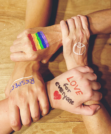 Beim Change Management geht es auch um ein Miteinander, hier dargestellt mit 4 Händen, die sich so umfassen, dass sie einen Kreis bilden. Auf den Handrücken Friedenssymbole und eine Regenbogenfahne