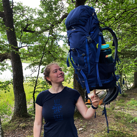 Junge Frau mit deuter Rucksack, den sie scheinbar auf nur einem Finger balanciert