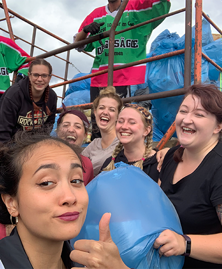 Team Scavenger Hunt Team bringt Müll zum Müllwagen und macht davor schnell noch ein Beweisfoto - lachend mit Daumen hoch