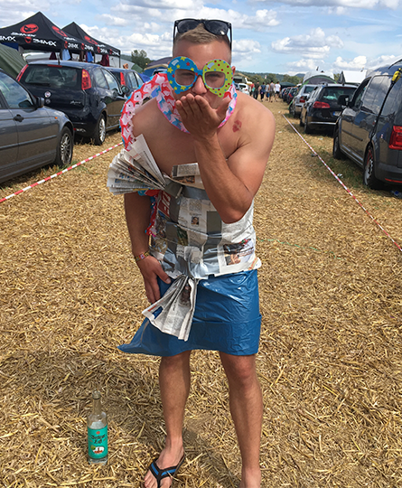 Junger Mann mit Outfit aus alter Zeitung und Müllsack trägt dazu noch witzige Papierbrille und -schal und wirft eine Kusshand