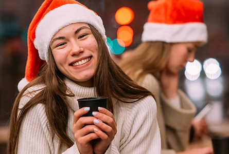 Dame mit Becher in der Hand und Weihnachtsmütze, freudiges Lächeln